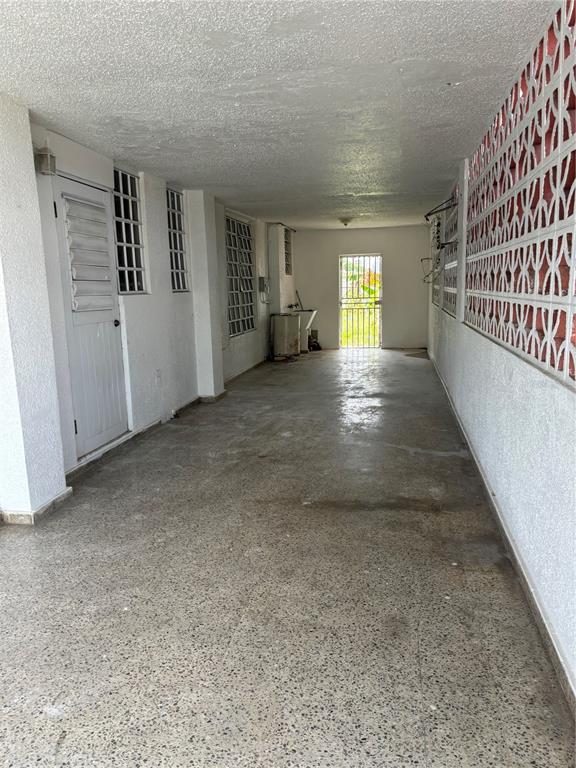 A long, covered concrete carport features white walls, a textured ceiling, and decorative breeze blocks — Calle 18 BLOQUE 23, BAYAMON, PR
