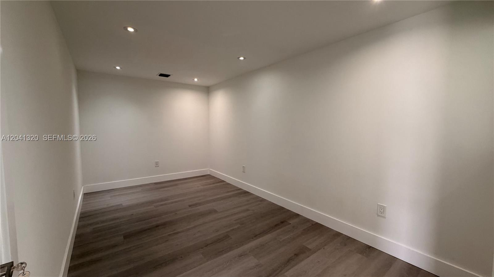 An empty room features white walls, recessed ceiling lights, and dark wood-look flooring — 8335 NW 64th St # 1, Medley FL 33166, MEDLEY, FL