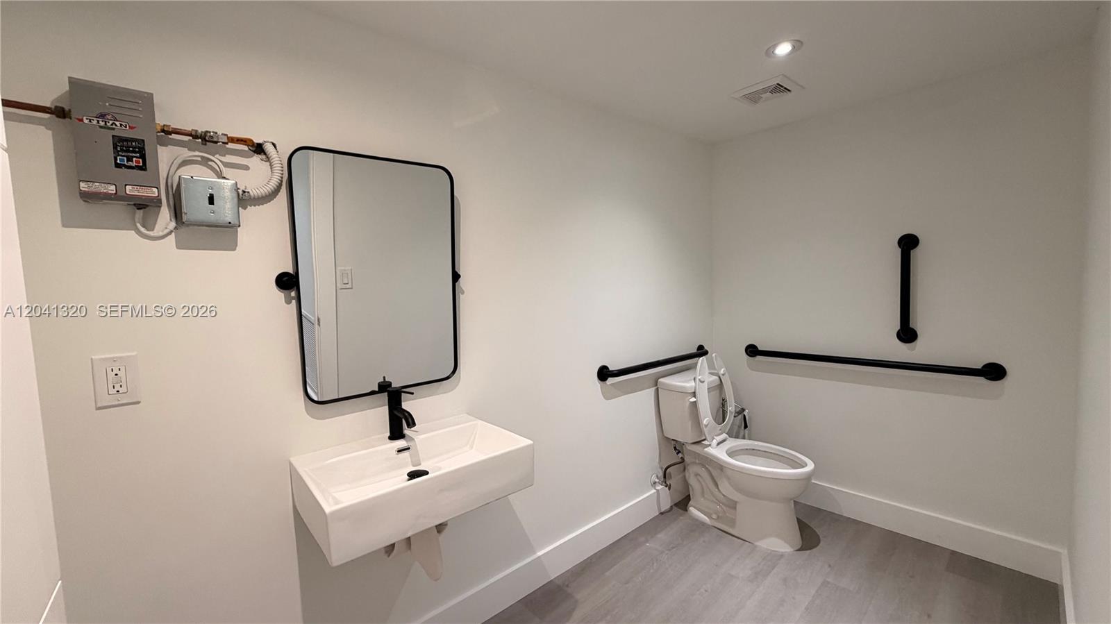 A modern bathroom features a wall-mounted sink, a toilet with grab bars, and exposed plumbing — 8335 NW 64th St # 1, Medley FL 33166, MEDLEY, FL