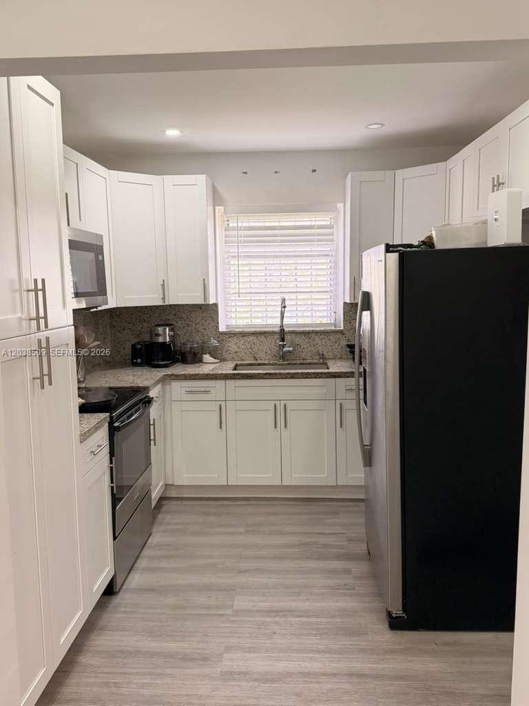 A galley-style kitchen features white cabinets, granite countertops, and stainless steel appliances — 2920 SW 15th St, Miami FL 33145, MIAMI, FL