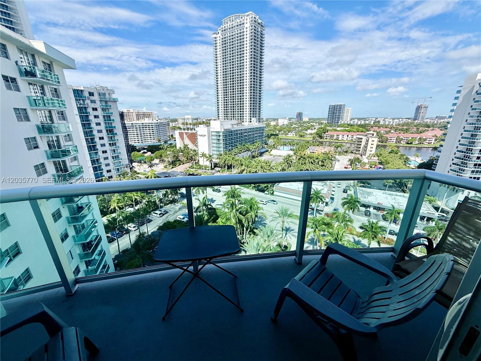 A balcony with a small table and chairs overlooks a city skyline and palm trees — 3901 S Ocean Dr # 14U, Hollywood FL 33019, HOLLYWOOD, FL