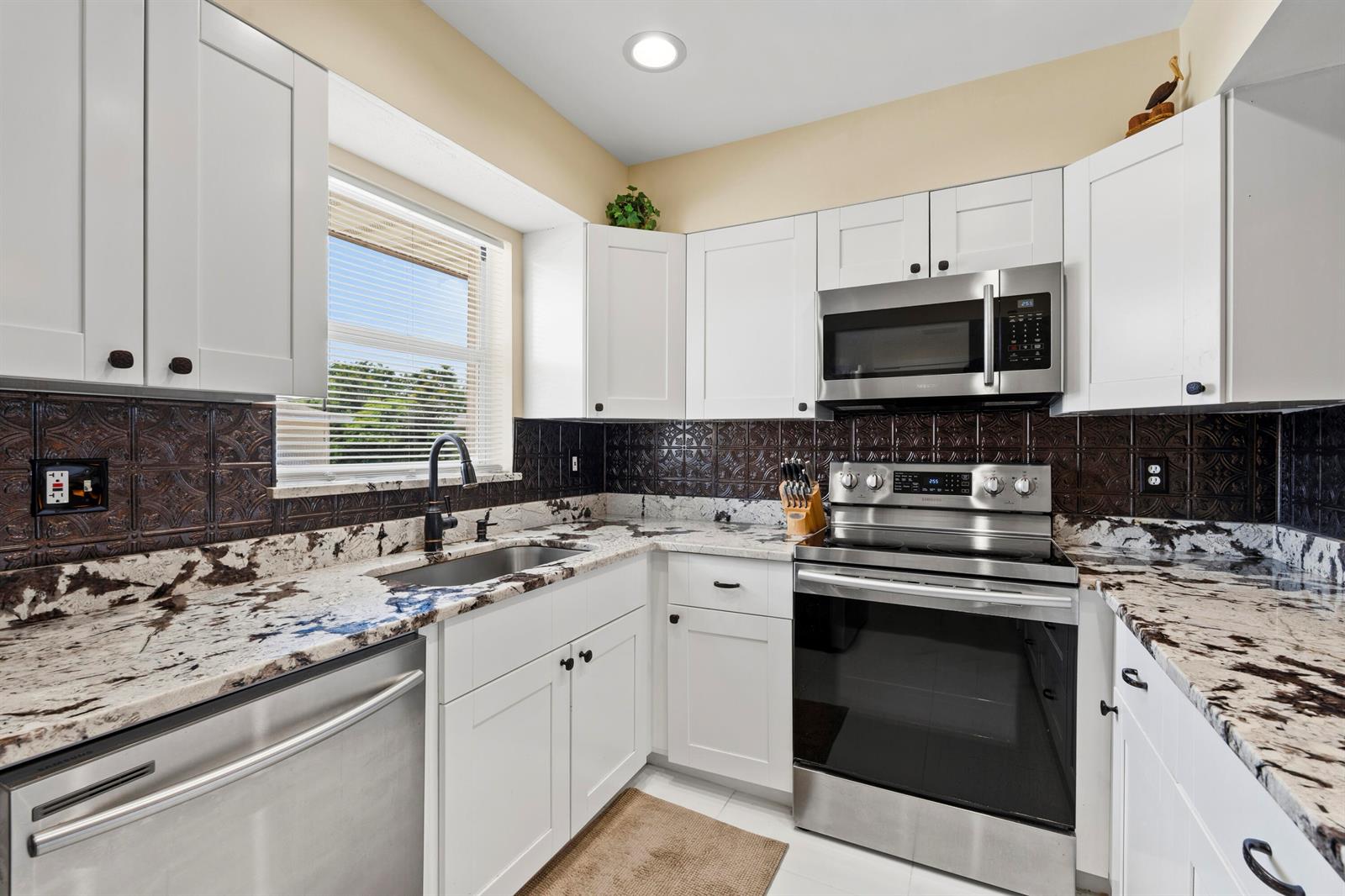 A kitchen features white cabinets, granite countertops, a dark patterned backsplash, and stainless steel appliances — 2950 SE Ocean Boulevard # 6, Stuart FL 34996, STUART, FL
