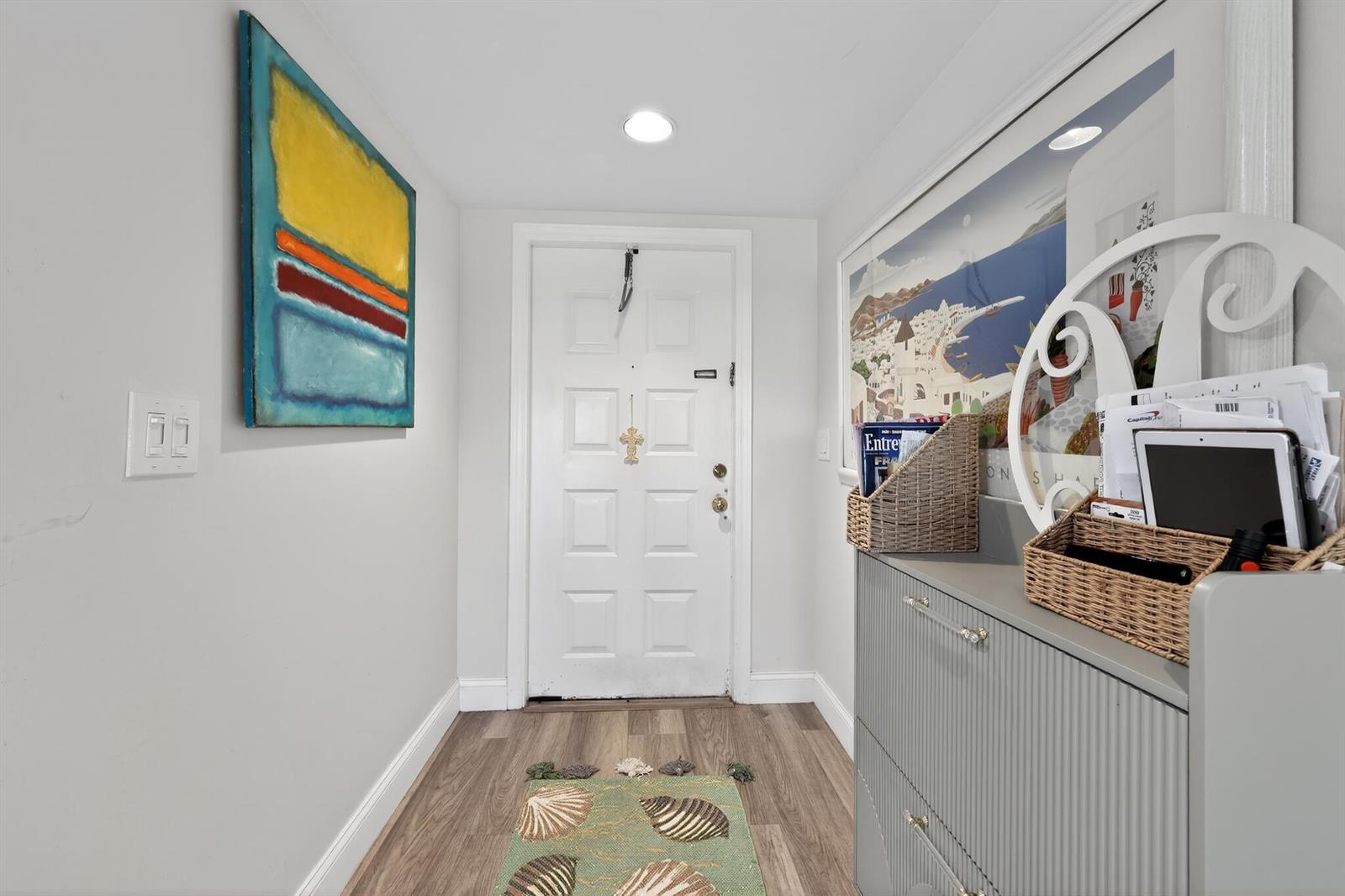 A bright entryway features a white door, wood-look flooring, a gray cabinet, and wall art — 2898 SW 22nd Circle # 231c, Delray Beach FL 33445, DELRAY BEACH, FL