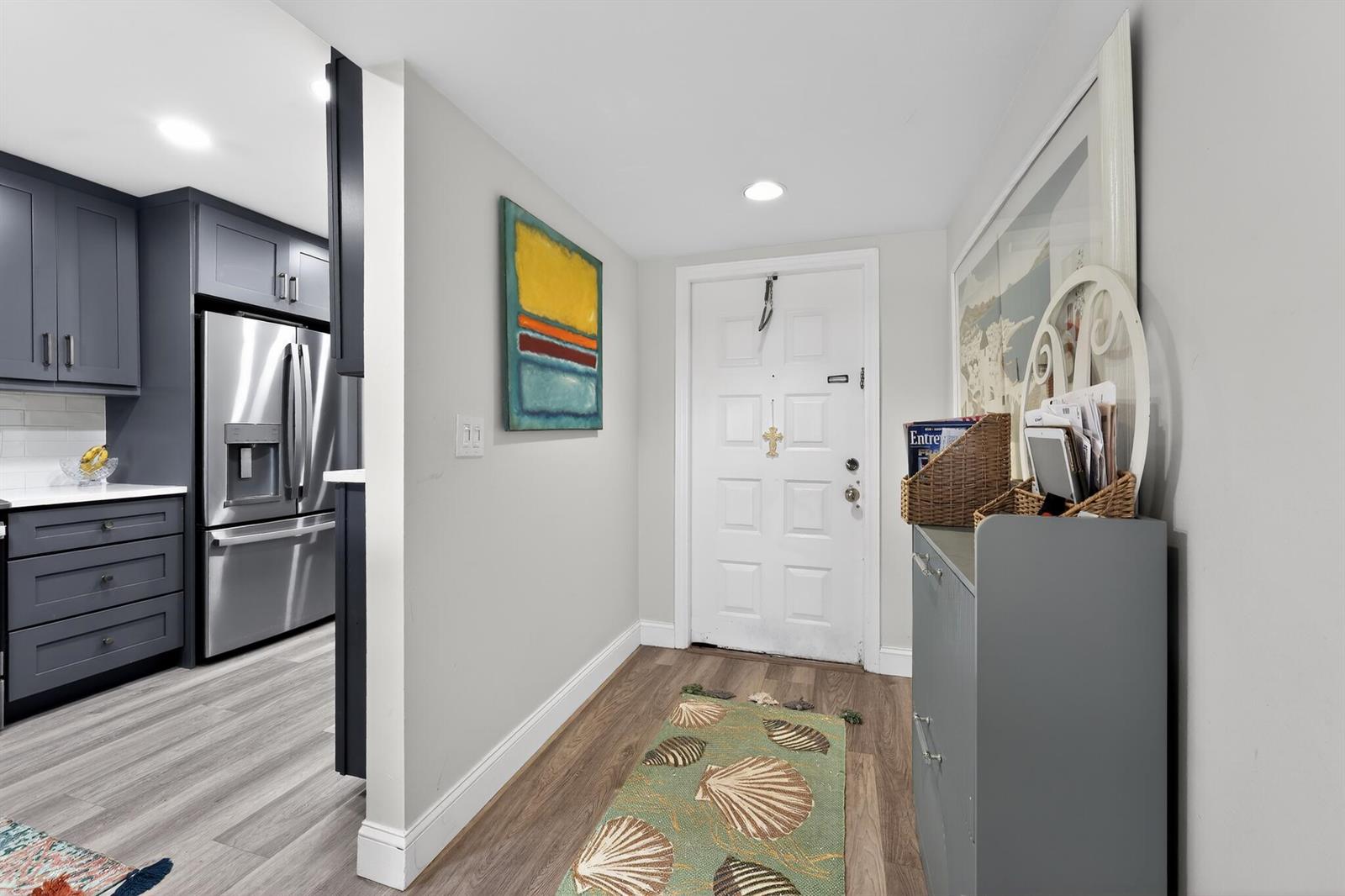 An entryway with a white door, a shell-patterned rug, and a view into a kitchen — 2898 SW 22nd Circle # 231c, Delray Beach FL 33445, DELRAY BEACH, FL