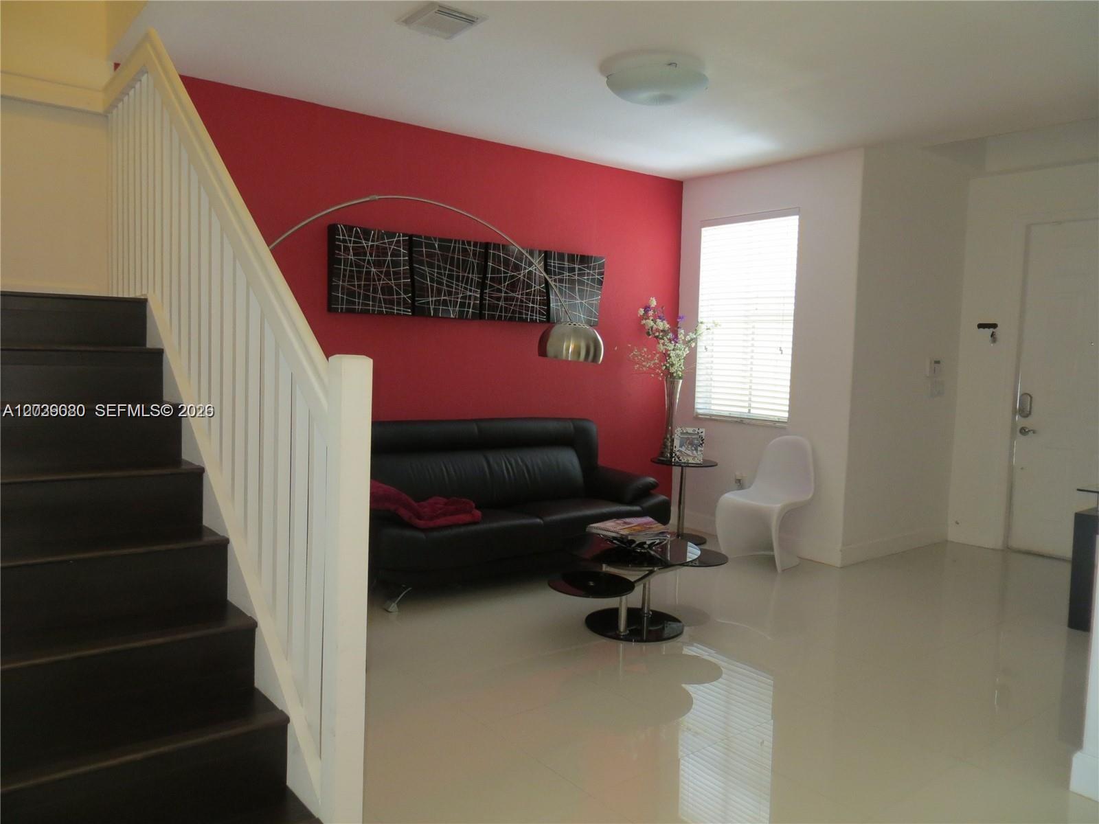 A living room features a red accent wall, black leather sofa, and dark wooden stairs — 7878 NW 110th Ave, Doral FL 33178, DORAL, FL