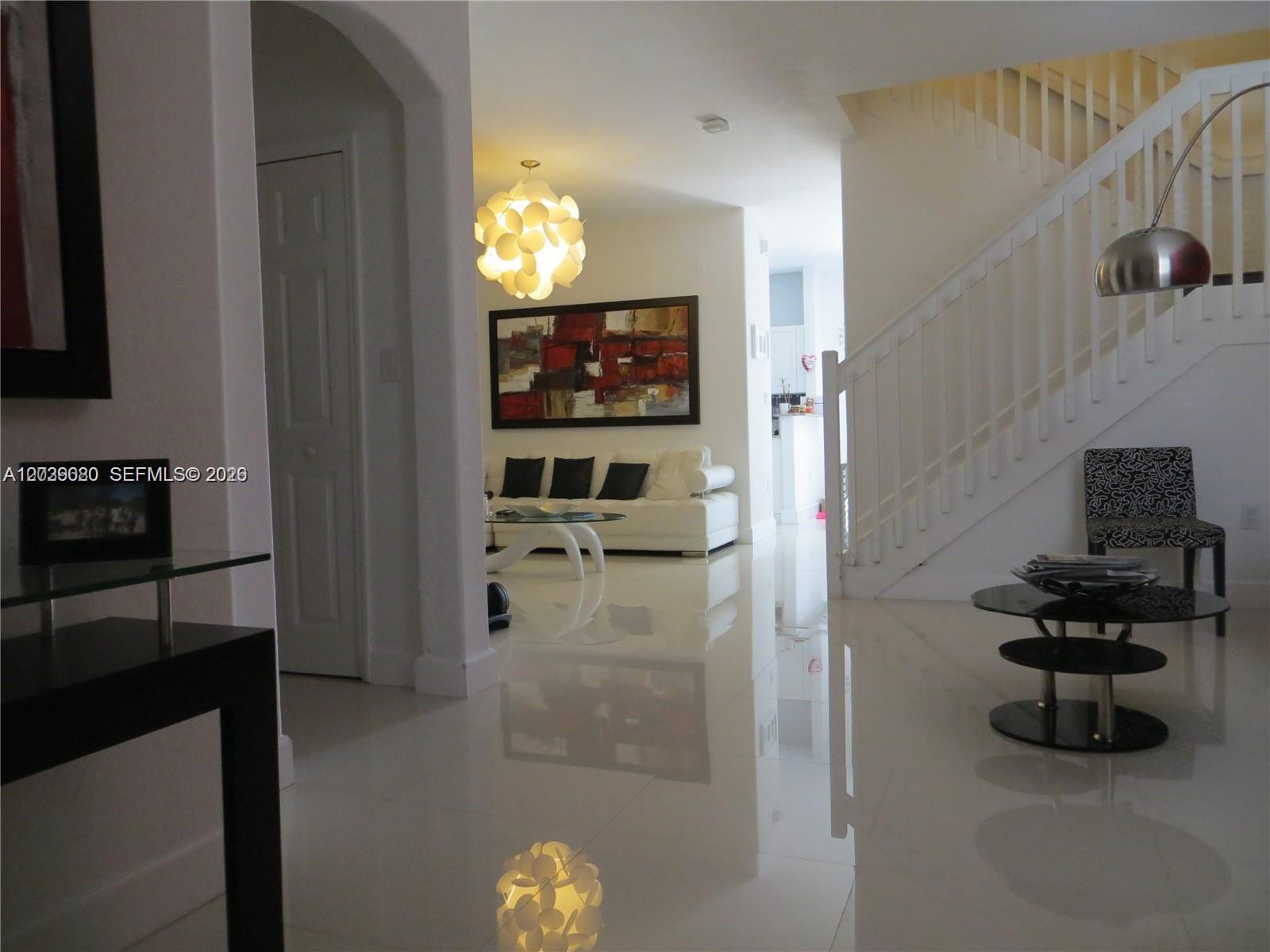 A bright living room features white tile floors, a staircase, and modern lighting fixtures — 7878 NW 110th Ave, Doral FL 33178, DORAL, FL