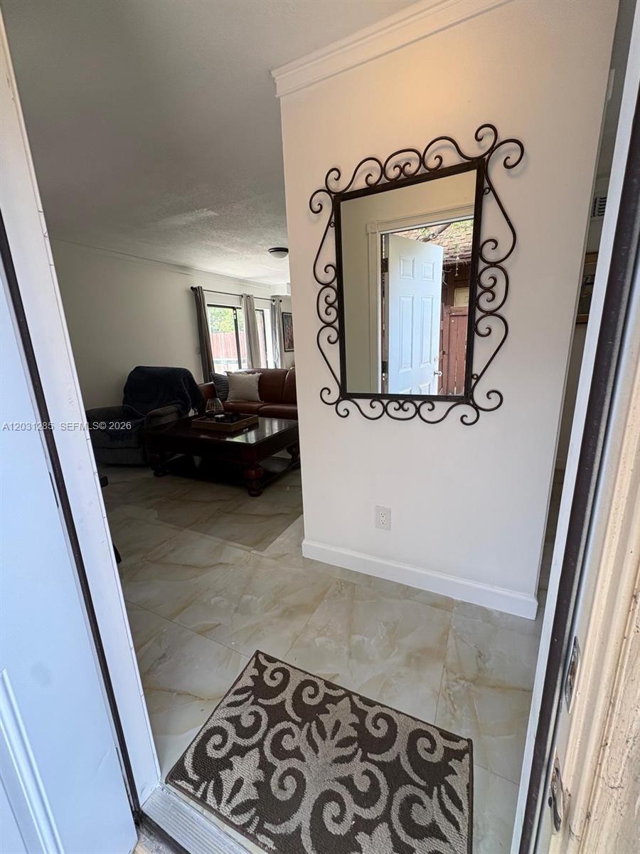 An entryway with tile flooring leads into a living room featuring a decorative wall mirror — 7104 SW 114th Pl # A, Miami FL 33173, MIAMI, FL