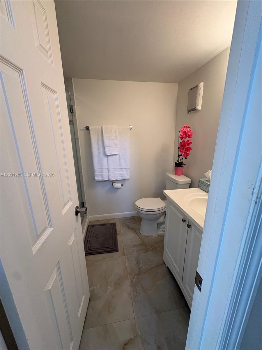 A small bathroom features a white vanity, a toilet, a shower, and light-colored tile flooring — 7104 SW 114th Pl # A, Miami FL 33173, MIAMI, FL