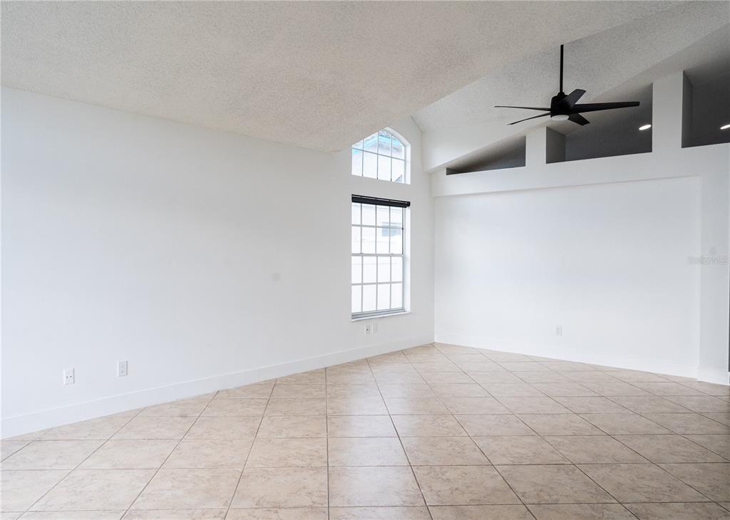 A bright, empty living room features white walls, tile flooring, and a vaulted ceiling — 2319 ISLAND CLUB WAY, ORLANDO, FL