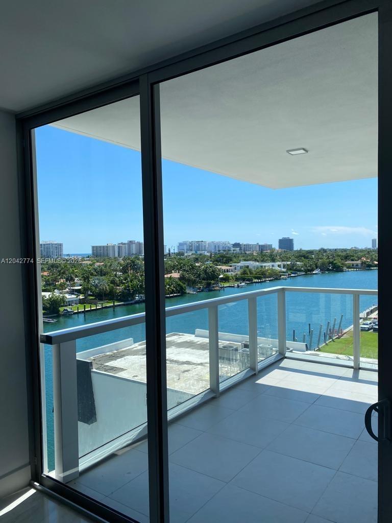 A balcony with glass railings overlooks a waterway, lush greenery, and distant city buildings — 9521 E Bay Harbor Dr # 605, Bay Harbor Islands FL 33154, BAY HARBOR ISLANDS, FL