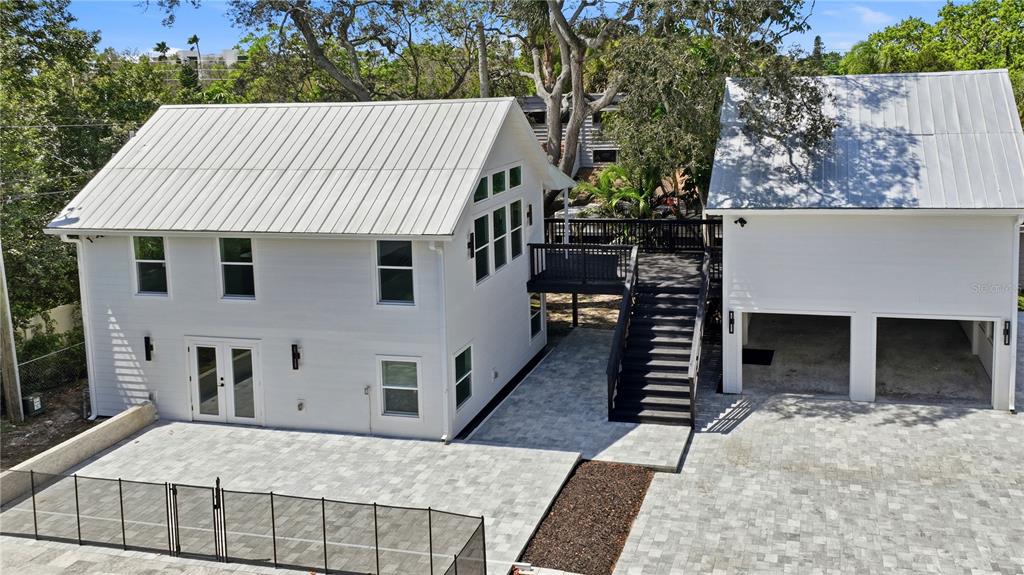 An exterior view of a white two-story house with a metal roof and paved patio — 1109 CHARLES STREET, CLEARWATER, FL