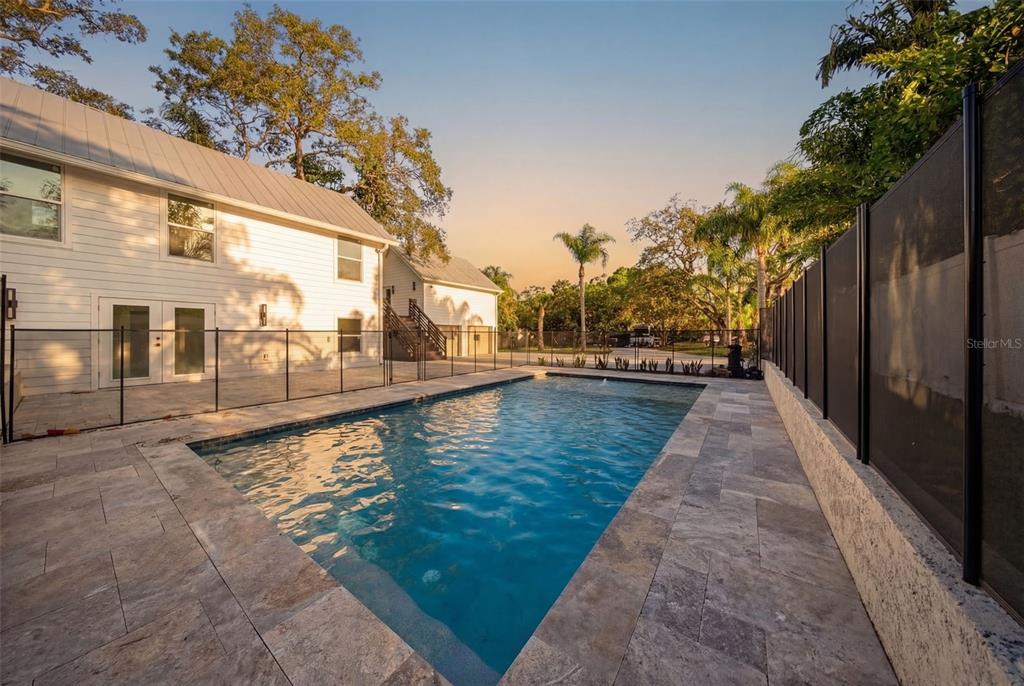 A rectangular swimming pool sits on a stone patio next to a white two-story house — 1109 CHARLES STREET, CLEARWATER, FL