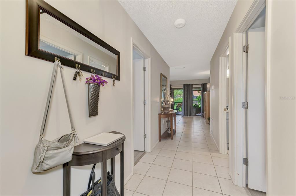 A bright hallway with light tile flooring leads toward a windowed living area — 5103 GREENCROFT ROAD, SARASOTA, FL