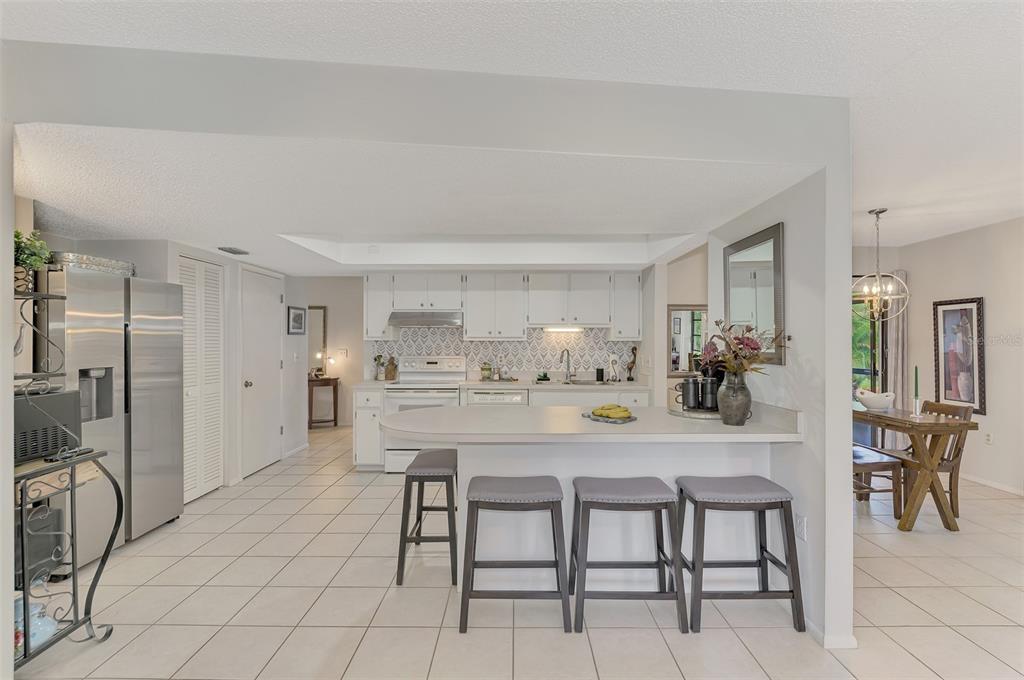 A kitchen with white cabinets, a breakfast bar with four stools, and tiled flooring — 5103 GREENCROFT ROAD, SARASOTA, FL