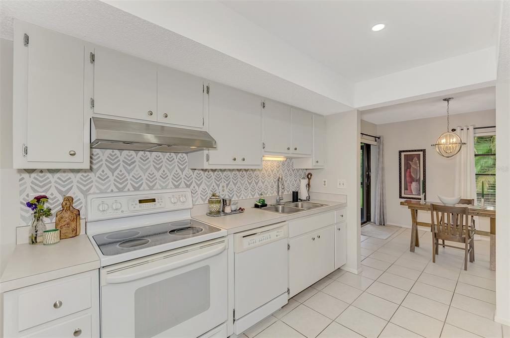 A kitchen with white cabinets, a patterned backsplash, and an adjacent dining area with tile — 5103 GREENCROFT ROAD, SARASOTA, FL