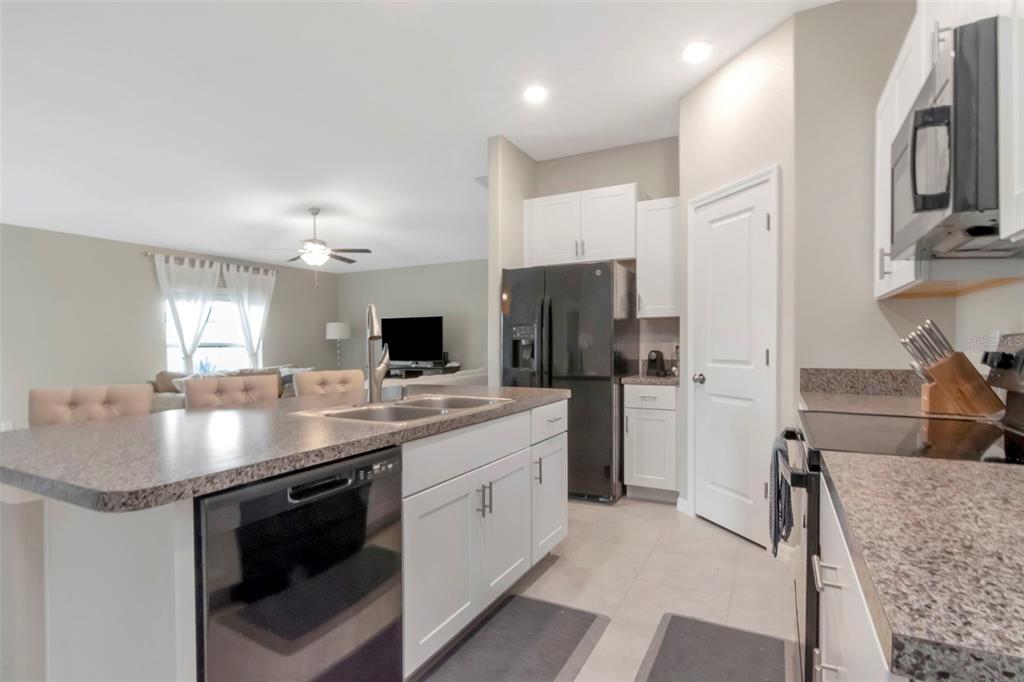 A kitchen with white cabinets, granite countertops, and a black dishwasher overlooks a living area — 11527 SAGE CANYON DRIVE, RIVERVIEW, FL