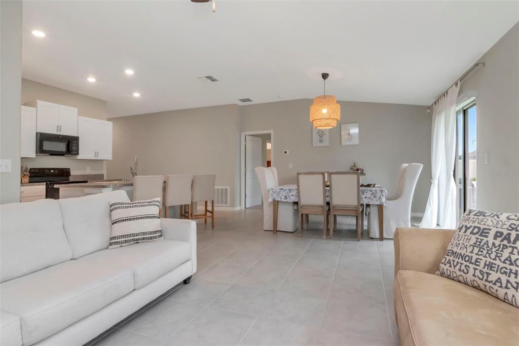 An open-concept living and dining area features white tile floors, neutral walls, and modern furniture — 11527 SAGE CANYON DRIVE, RIVERVIEW, FL