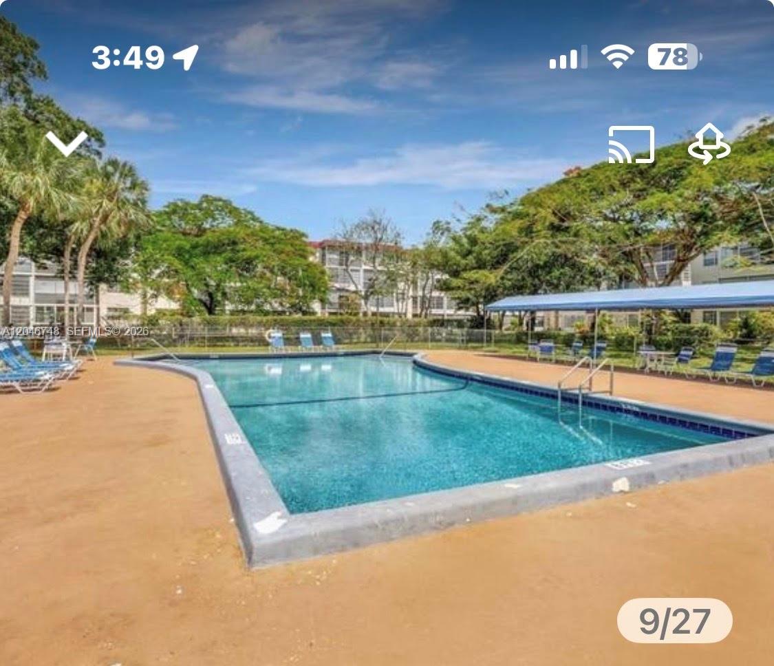 An outdoor swimming pool with a blue canopy and lounge chairs surrounded by lush trees — LAUDERDALE LAKES, FL
