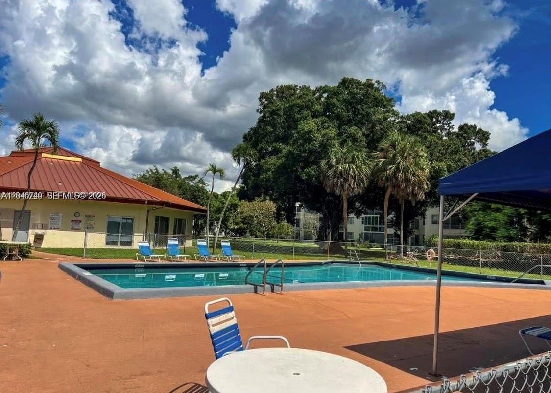 An outdoor swimming pool with lounge chairs and a clubhouse under a cloudy blue sky — LAUDERDALE LAKES, FL