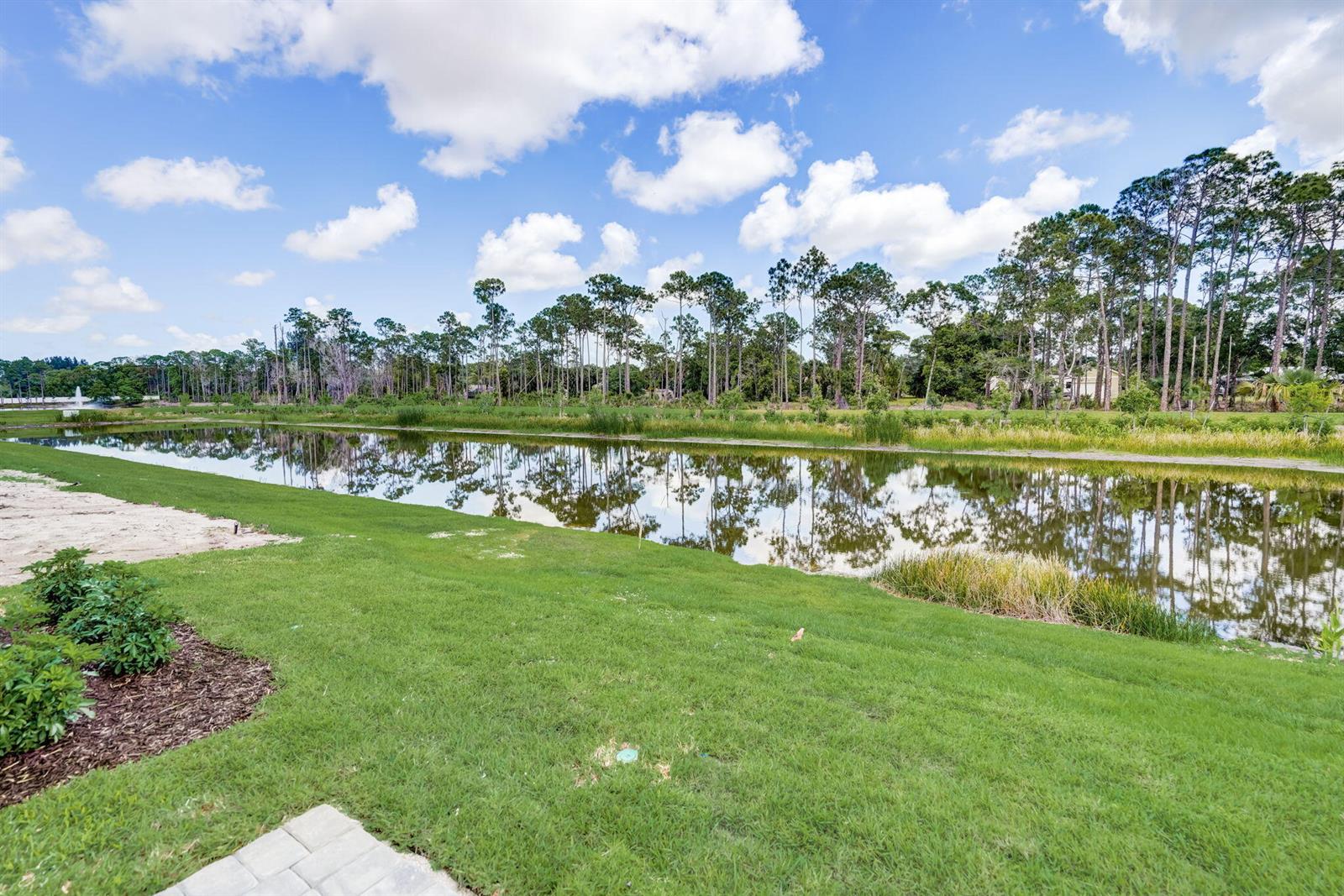 A grassy lawn overlooks a calm pond bordered by a line of tall pine trees — 5728 SE Edgewater Circle, Stuart FL 34997, STUART, FL