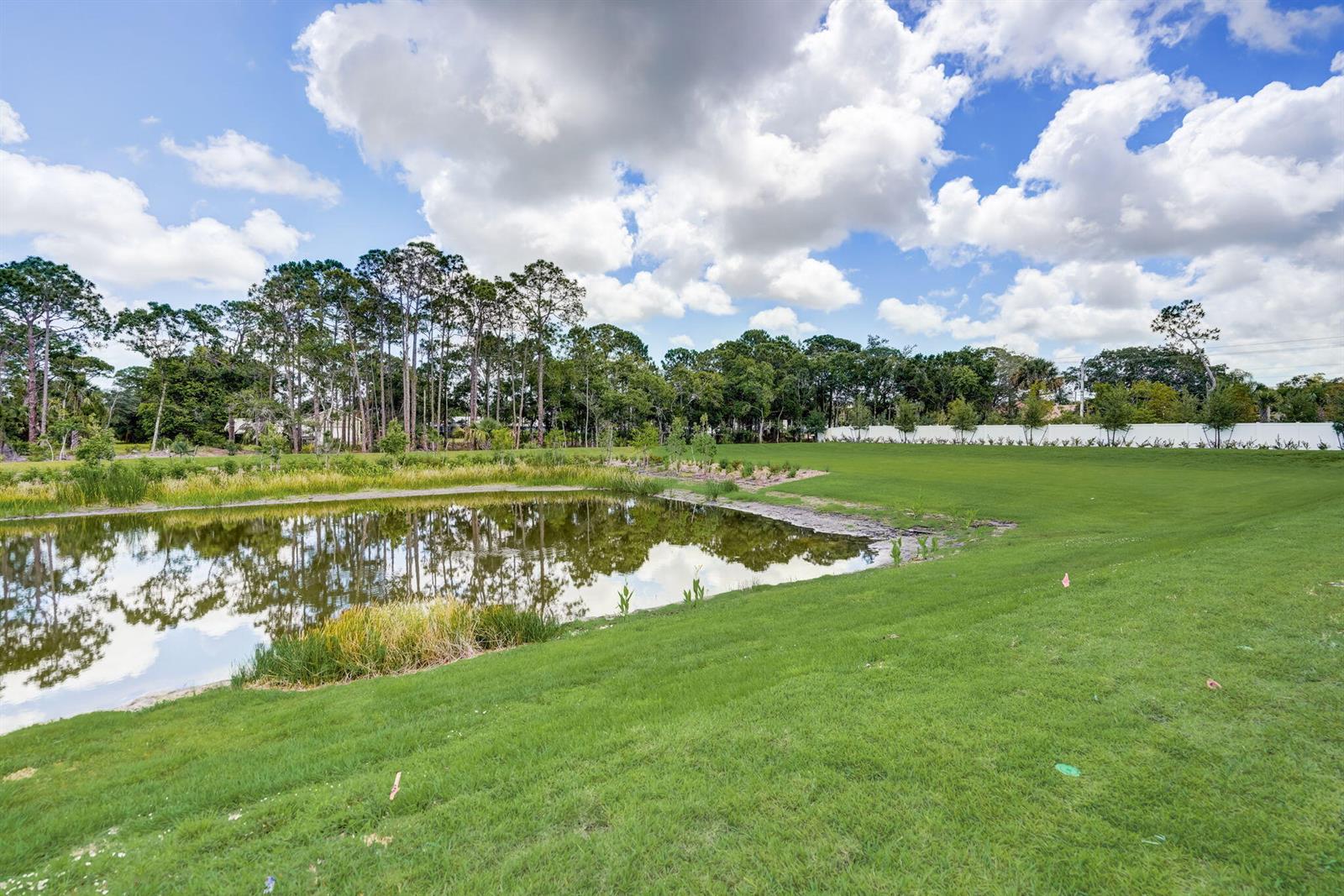 A grassy lawn slopes down to a small pond bordered by trees under a cloudy sky — 5728 SE Edgewater Circle, Stuart FL 34997, STUART, FL