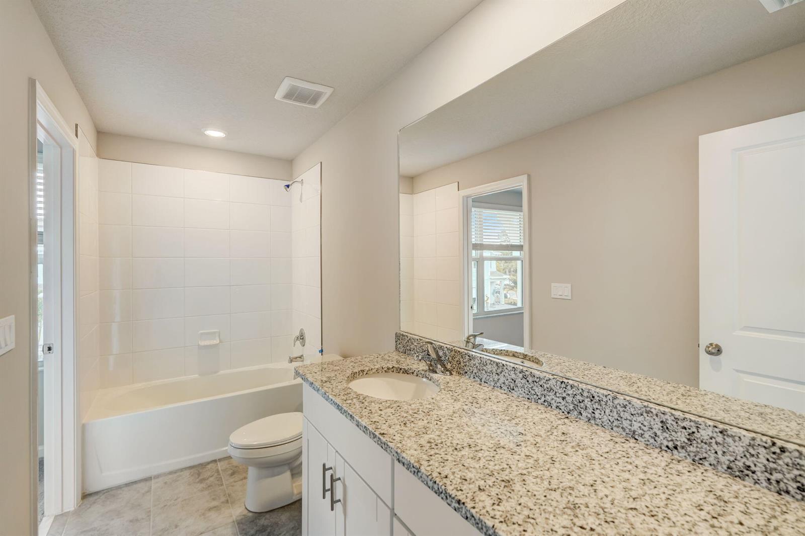 A bathroom features a white vanity with granite countertops, a toilet, and a shower-tub combo — 5728 SE Edgewater Circle, Stuart FL 34997, STUART, FL