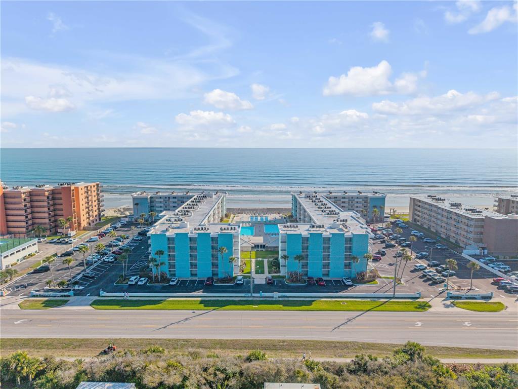 An aerial view shows a blue multi-story apartment complex situated directly along the oceanfront — 4153 S ATLANTIC AVENUE UNIT 1170, NEW SMYRNA BEACH, FL