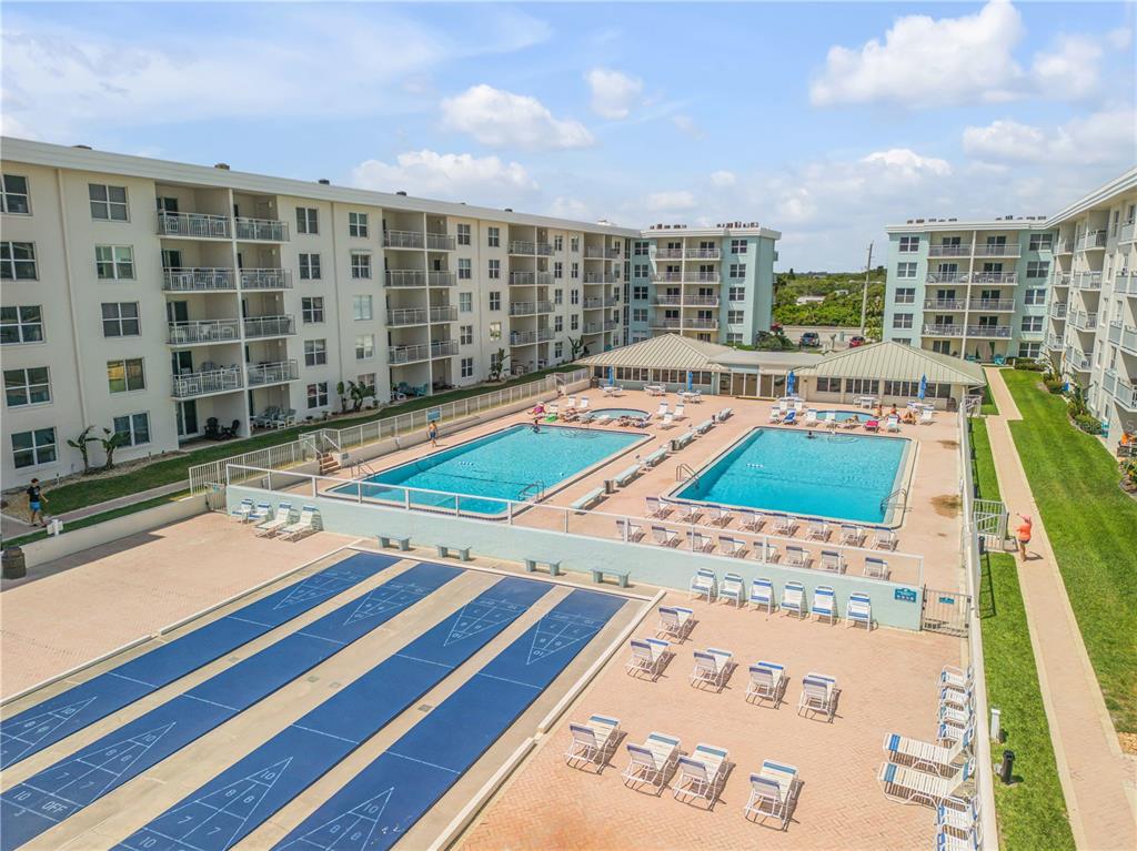 An aerial view shows two swimming pools, shuffleboard courts, and multi-story residential apartment buildings — 4153 S ATLANTIC AVENUE UNIT 1170, NEW SMYRNA BEACH, FL