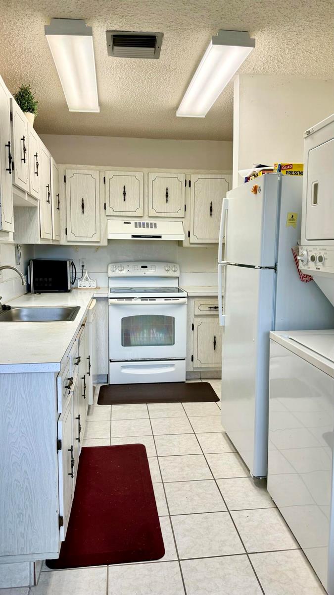 A galley-style kitchen features white cabinets, white appliances, tiled flooring, and dual overhead light fixtures — 1551 NW 20th Avenue # 102, Delray Beach FL 33445, DELRAY BEACH, FL