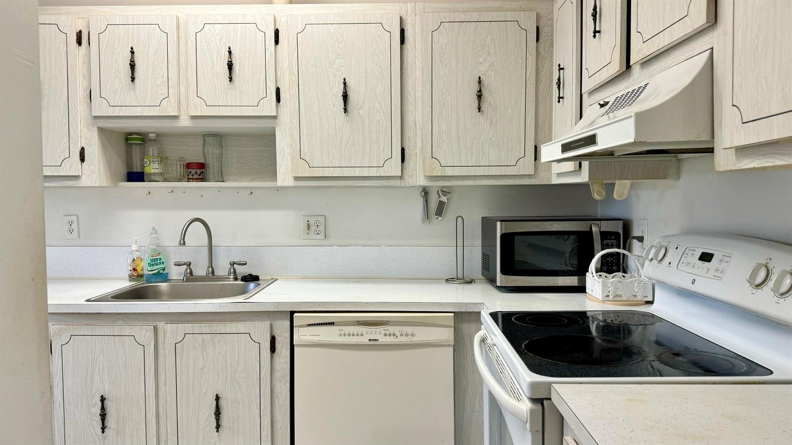 A kitchen features light wood-grain cabinets, white countertops, a stainless steel sink, and white appliances — 1551 NW 20th Avenue # 102, Delray Beach FL 33445, DELRAY BEACH, FL