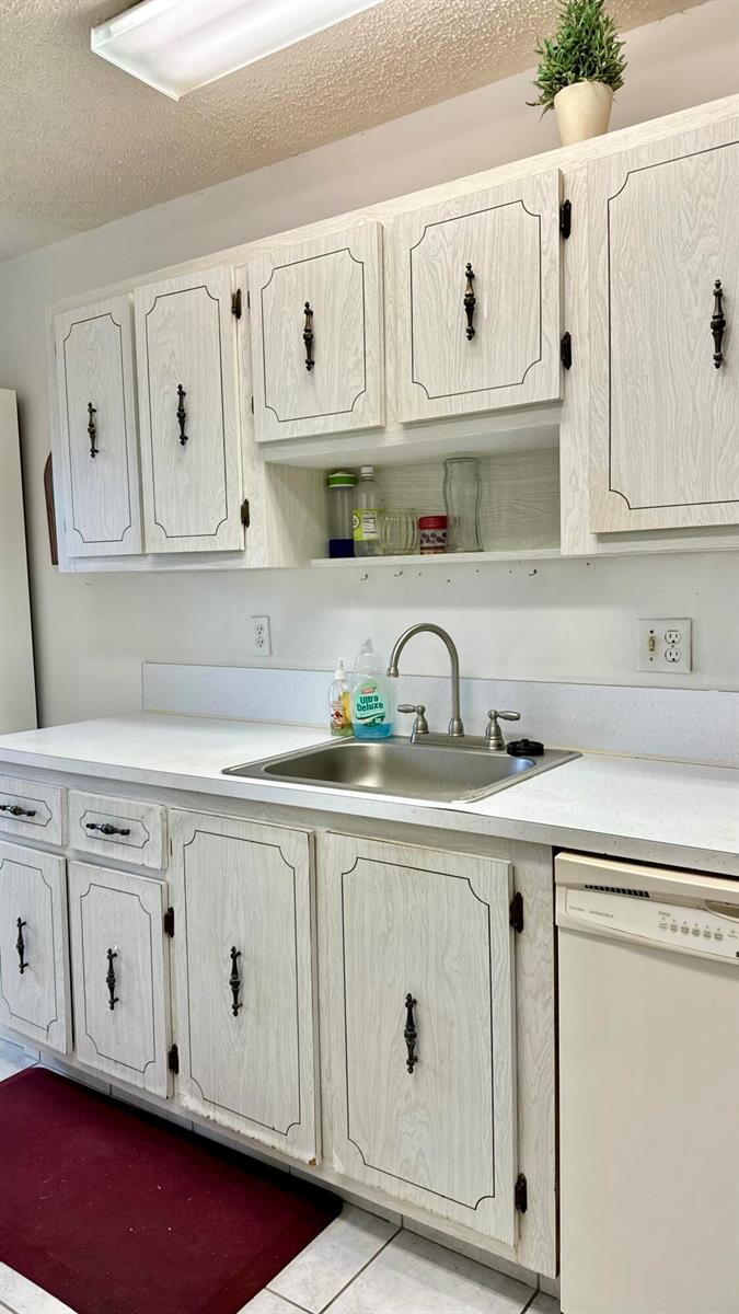 A kitchen features white wood-grain cabinets with black hardware, a stainless steel sink, and countertops — 1551 NW 20th Avenue # 102, Delray Beach FL 33445, DELRAY BEACH, FL