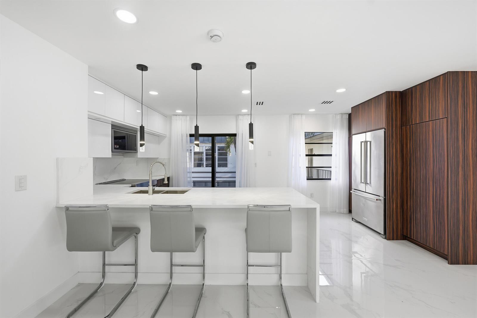 A modern kitchen features a white marble island, gray bar stools, and dark wood cabinetry — 571 Piedmont L, Delray Beach FL 33484, DELRAY BEACH, FL