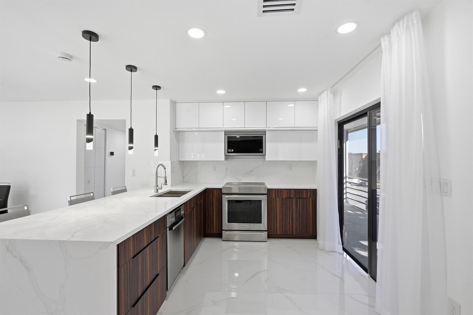 A modern kitchen features dark wood cabinets, white marble countertops, stainless steel appliances, and pendant lighting — 571 Piedmont L, Delray Beach FL 33484, DELRAY BEACH, FL