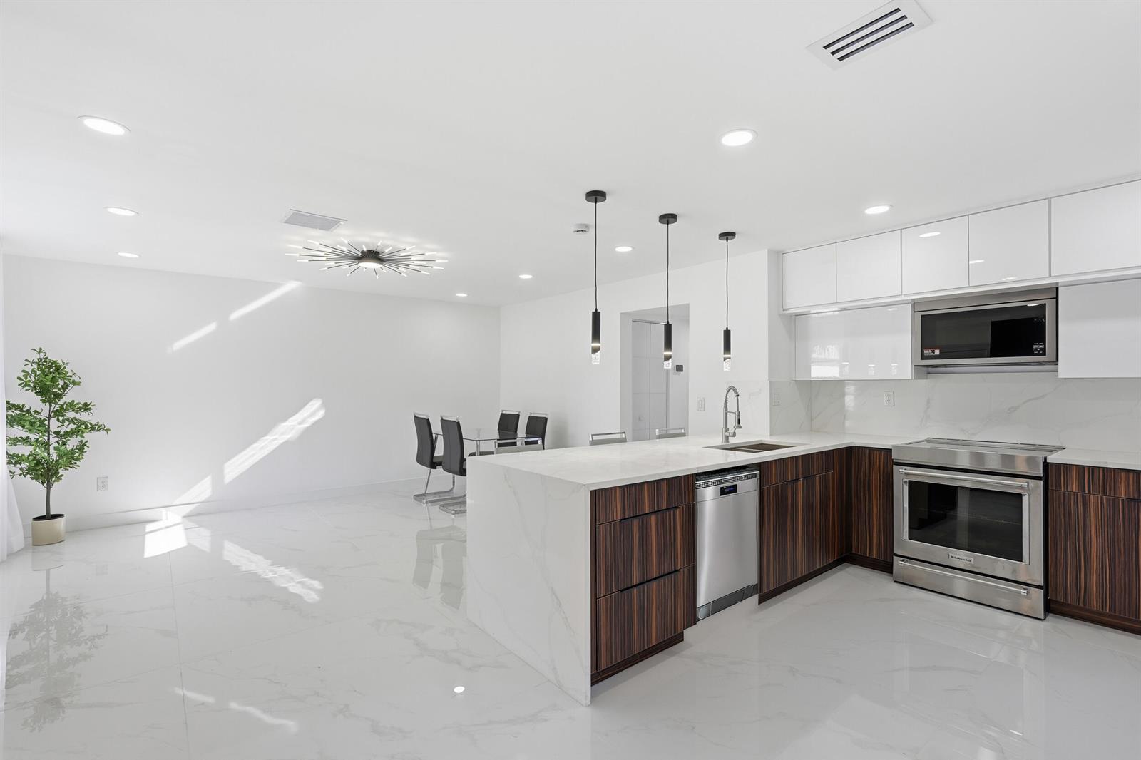 A modern kitchen features dark wood cabinetry, white marble countertops, and a dining area — 571 Piedmont L, Delray Beach FL 33484, DELRAY BEACH, FL