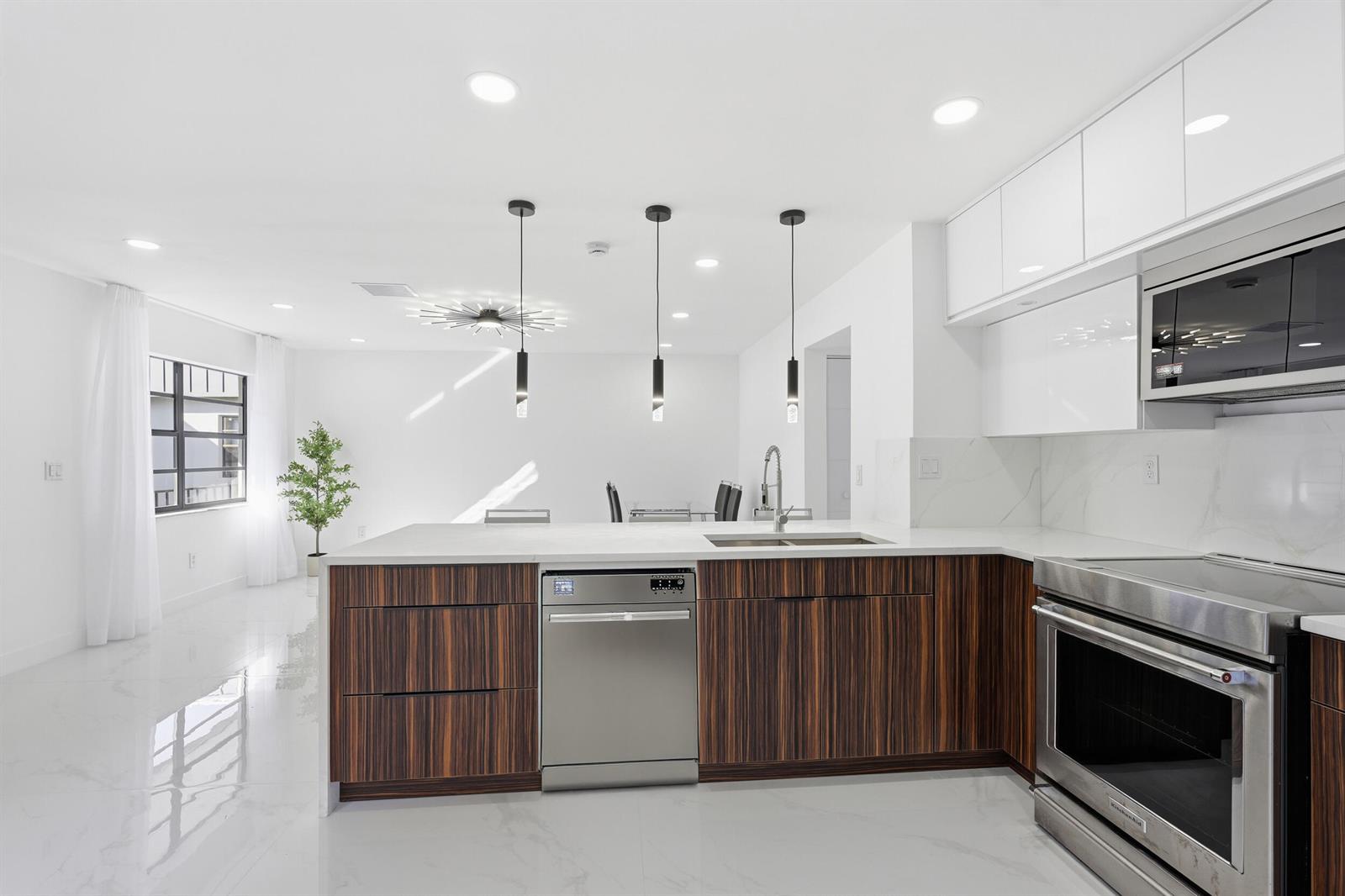 A modern kitchen features wood-grain cabinets, stainless steel appliances, and a white marble-topped island — 571 Piedmont L, Delray Beach FL 33484, DELRAY BEACH, FL