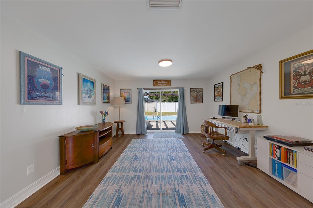 A room with wood-look flooring, a desk, a media console, and sliding doors to a pool — 4228 BRIARBERRY LANE, TAMPA, FL