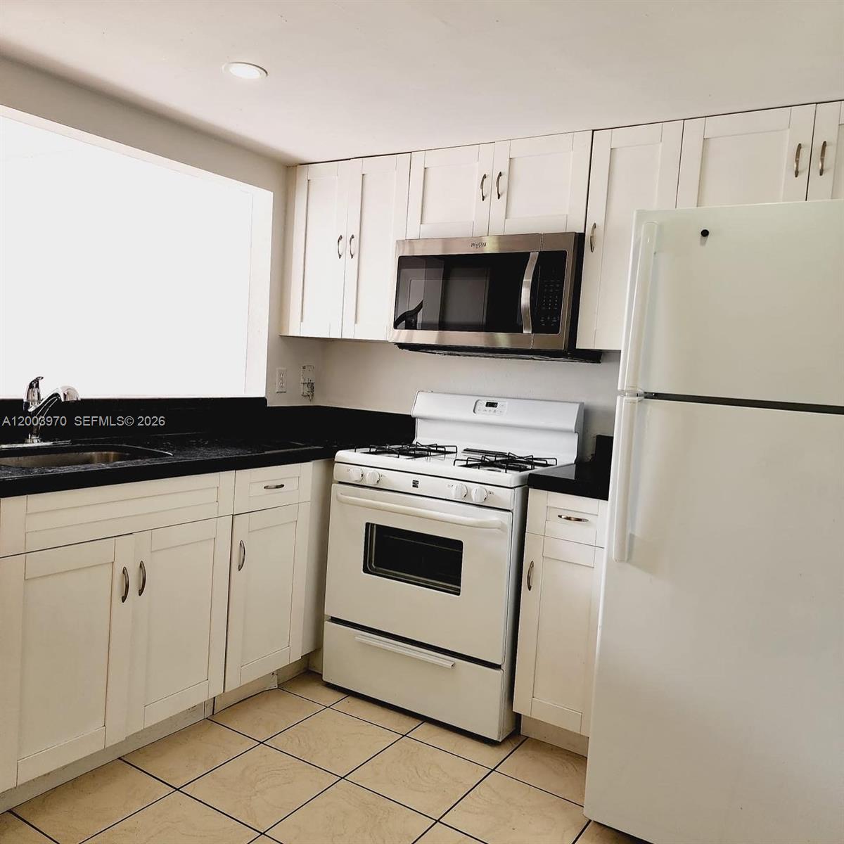 A kitchen features white cabinets, black countertops, a white stove, and a stainless steel microwave — 18051 NW 68th Ave # K202, Hialeah FL 33015, HIALEAH, FL