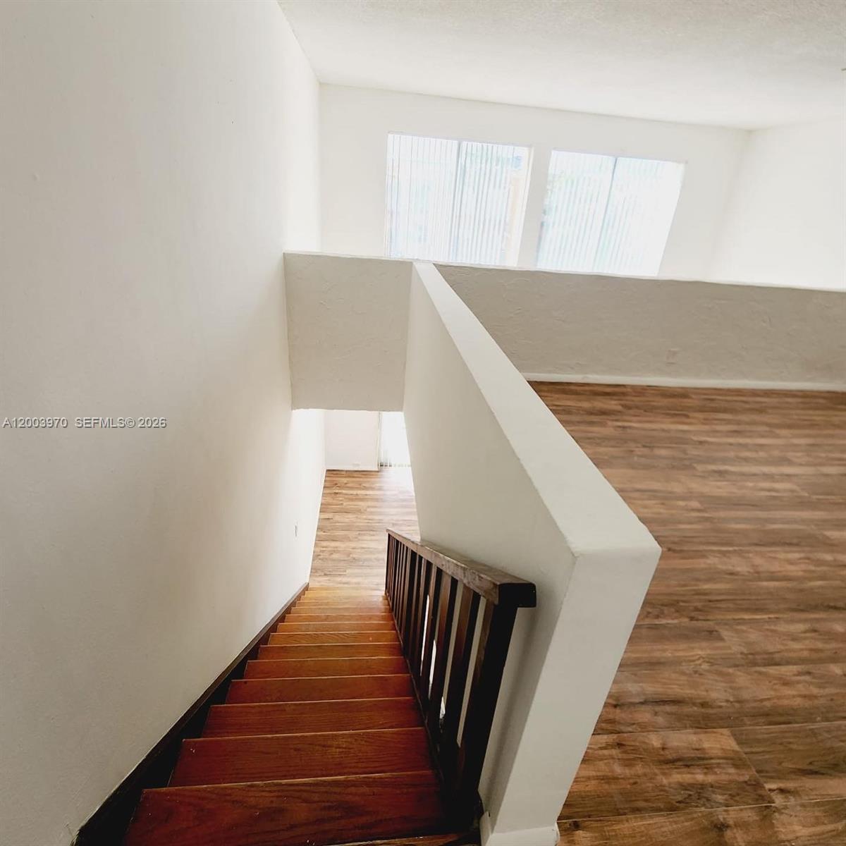 A wooden staircase leads down from a loft area with wood-look flooring and windows — 18051 NW 68th Ave # K202, Hialeah FL 33015, HIALEAH, FL