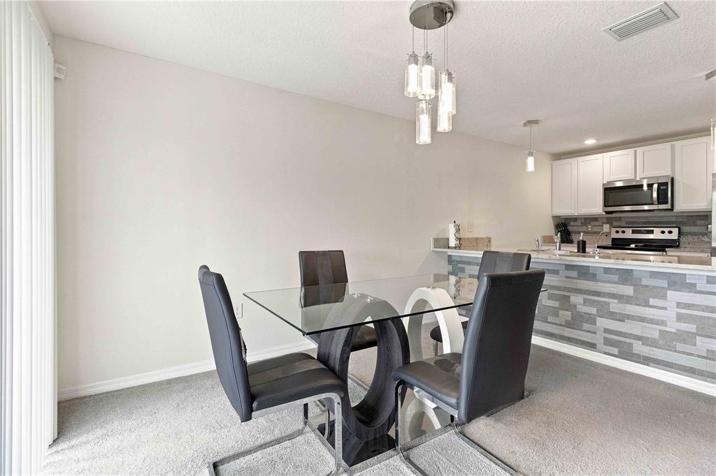 A dining area with a glass table and four chairs sits before an open kitchen — 2496 RIM DRIVE, SPRING HILL, FL