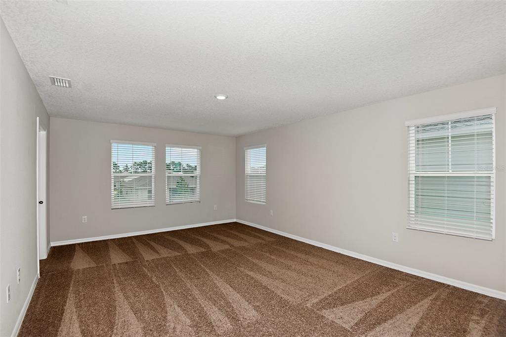 An empty room with beige walls, brown carpet, and several windows with white blinds — 34993 ARBOR RETREAT DRIVE, DADE CITY, FL