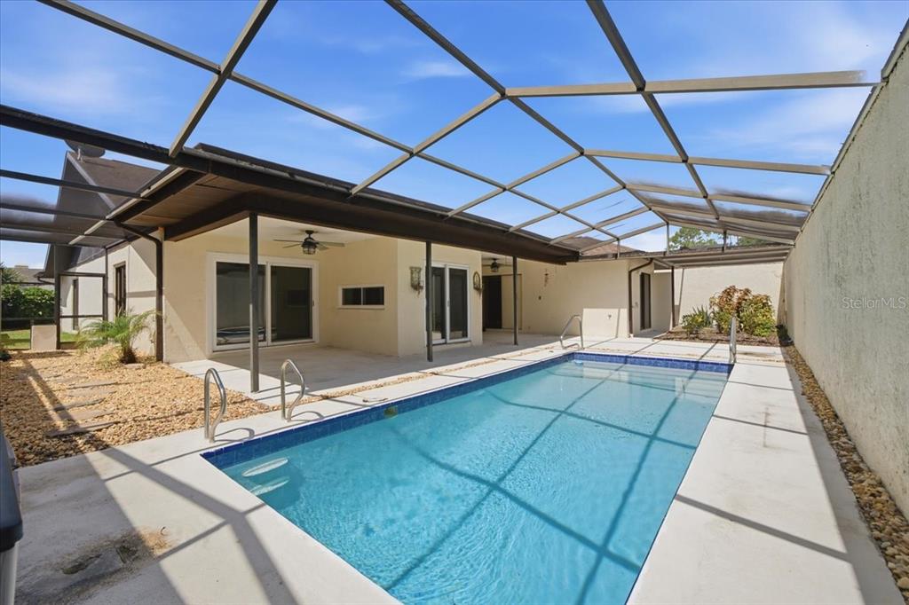 A rectangular swimming pool sits inside a screened-in patio area next to a house — 13510 AVISTA DRIVE, TAMPA, FL