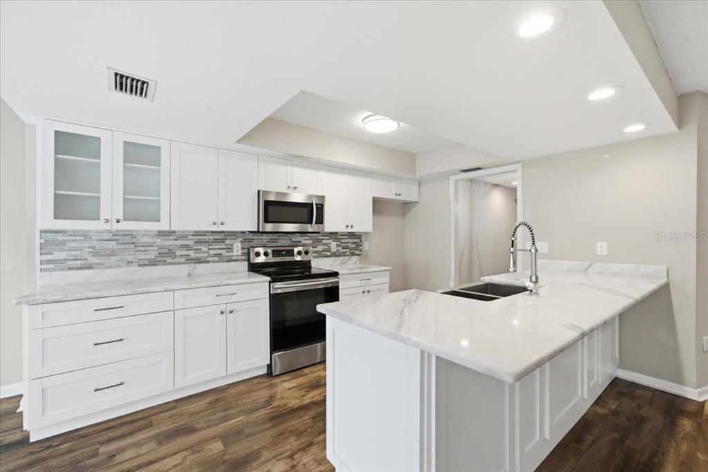 A modern kitchen features white cabinets, marble countertops, stainless steel appliances, and wood-look flooring — 13510 AVISTA DRIVE, TAMPA, FL