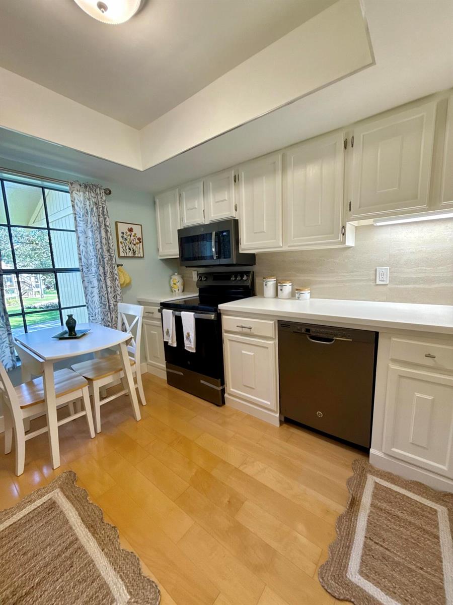 A kitchen features white cabinets, a black stove, a dishwasher, and a small dining area — 18390 SE Wood Haven Lane, Jupiter FL 33469, JUPITER, FL
