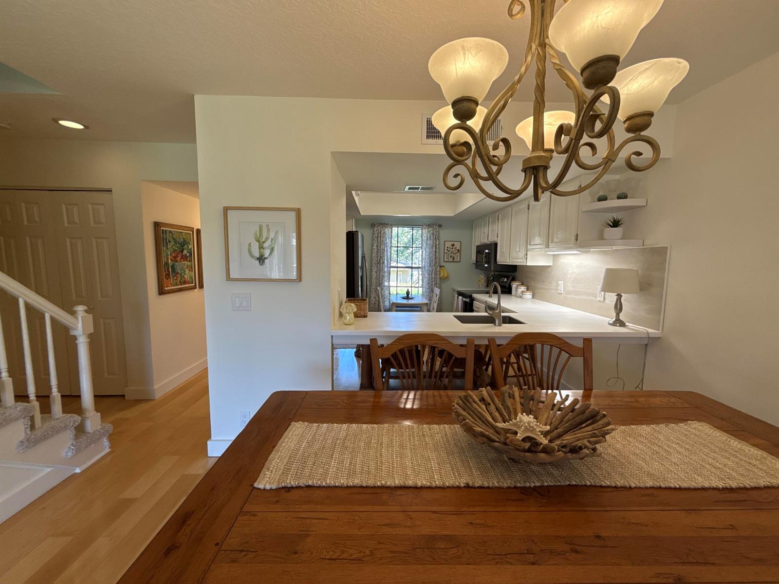 A dining area with a wooden table and chandelier overlooks a kitchen with white cabinets — 18390 SE Wood Haven Lane, Jupiter FL 33469, JUPITER, FL