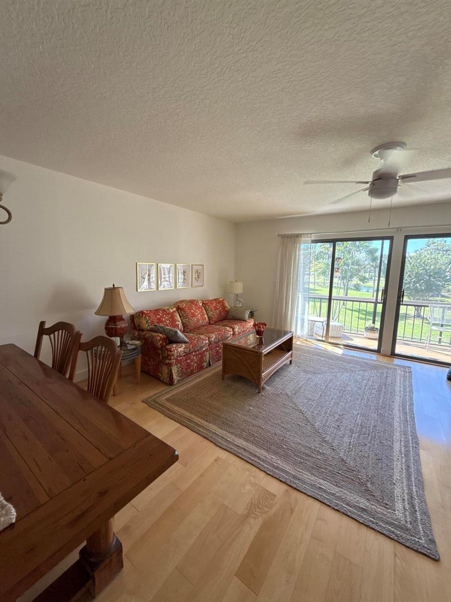 A living room with a floral sofa, wooden dining table, and sliding glass doors to a balcony — 18390 SE Wood Haven Lane, Jupiter FL 33469, JUPITER, FL