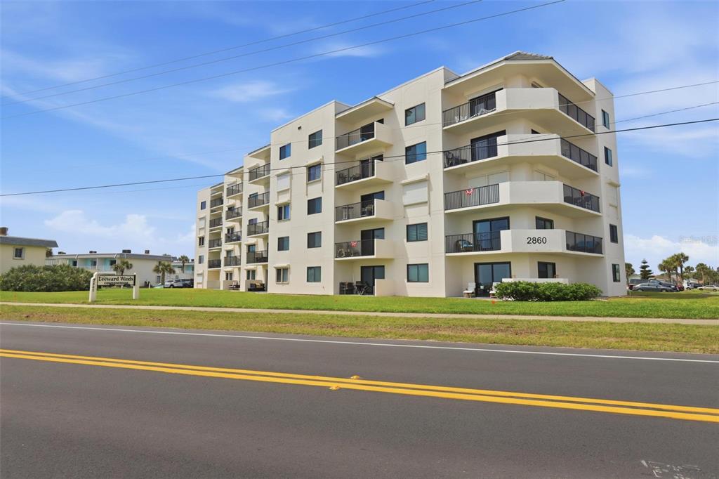 A multi-story white condominium building stands beside a road under a blue sky — 2860 OCEAN SHORE BOULEVARD UNIT 3030, ORMOND BY THE SEA, FL