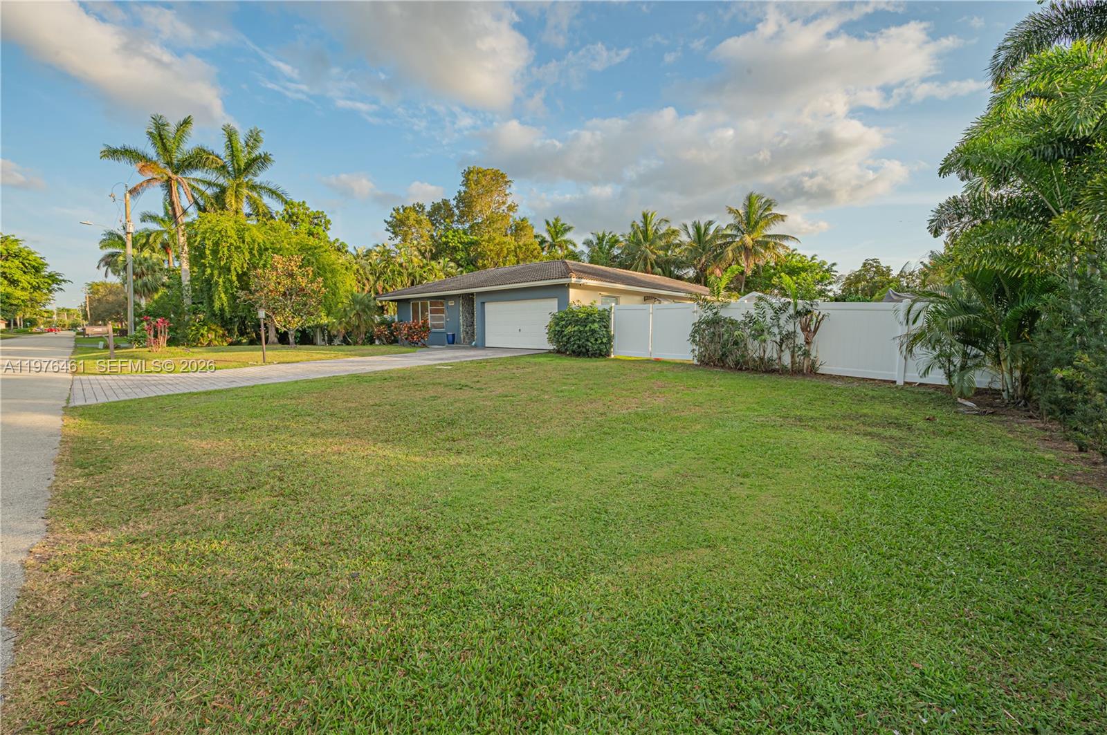 A single-story house with a white fence and a large front lawn under a blue sky — 11400 Tara Dr, Plantation FL 33325, PLANTATION, FL