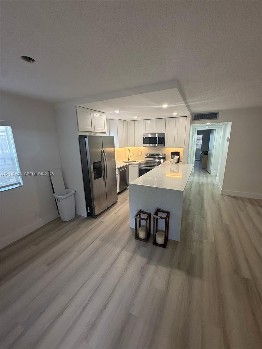 A modern kitchen features white cabinetry, stainless steel appliances, and a quartz-topped island — 200 E Monaco  E # 200, Delray Beach FL 33446, DELRAY BEACH, FL