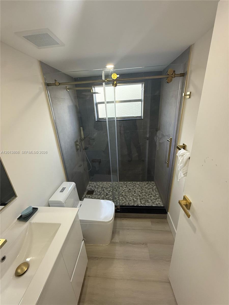 A bathroom features a glass-enclosed shower with pebble flooring, a white vanity, and gold fixtures — 200 E Monaco  E # 200, Delray Beach FL 33446, DELRAY BEACH, FL