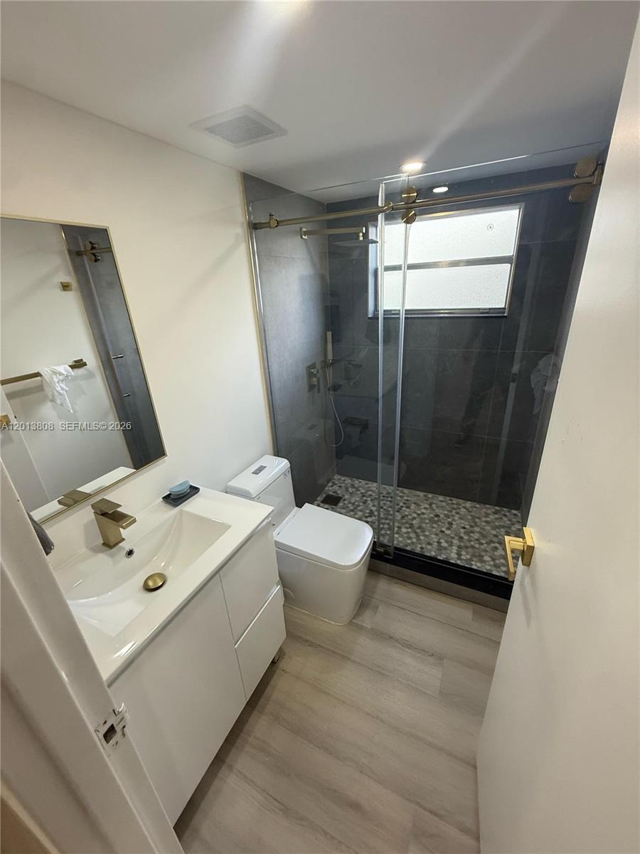 A modern bathroom features a white vanity, a glass-enclosed shower, and light wood-look flooring — 200 E Monaco  E # 200, Delray Beach FL 33446, DELRAY BEACH, FL